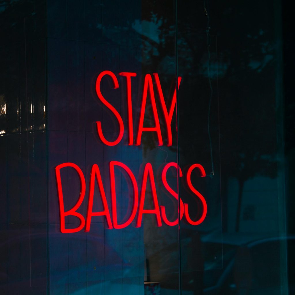 Vibrant red neon sign 'Stay Badass' glowing against a dark reflective surface.